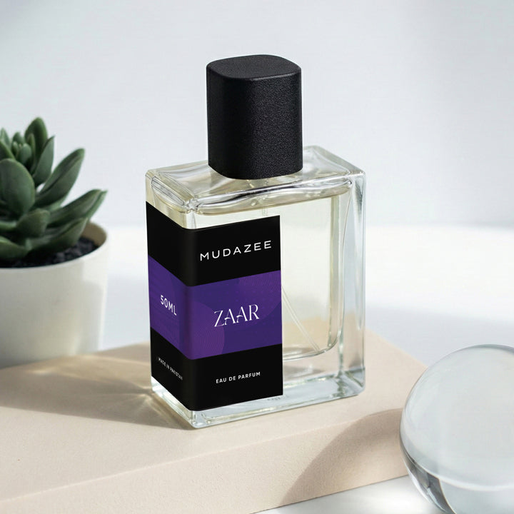 Mudazee Zaar perfume bottle on a light surface with a plant in the background